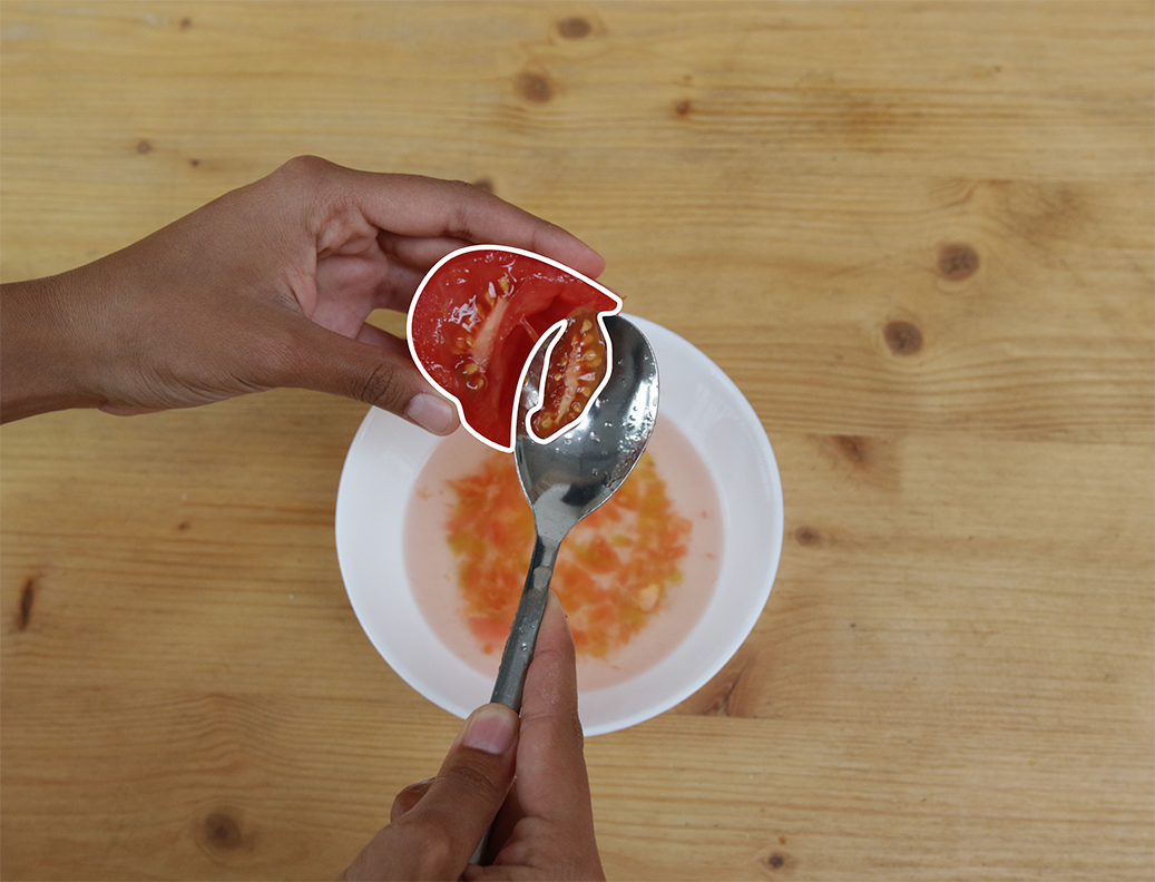 Une main dépose la pulpe de tomate avec une cuillère dans un bol d’eau.