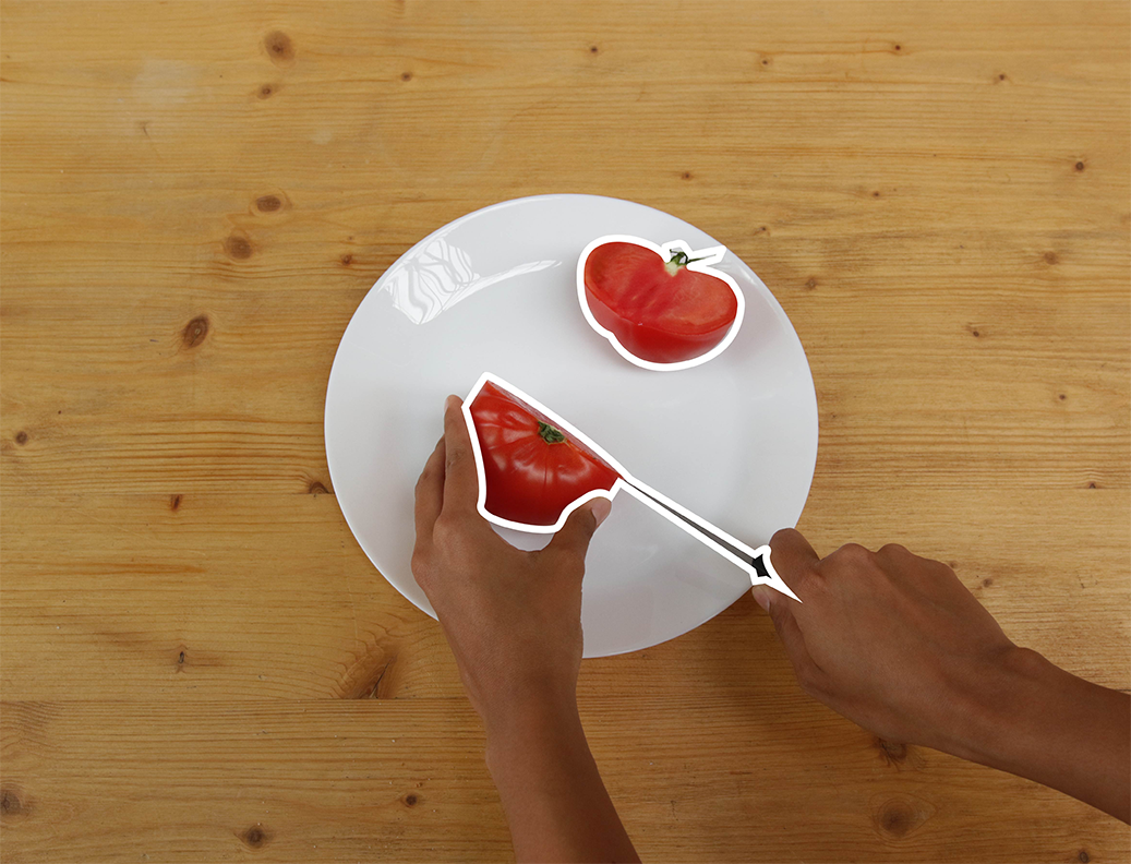 Des mains coupent une tomate en deux sur une assiette.